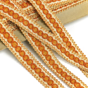 Könnte beinhalten: Nahaufnahme einer beige-orangenen Borte mit einem sich wiederholenden Muster aus kleinen Kreisen. Die Borte ist gefaltet und auf einer braunen Oberfläche gestapelt.