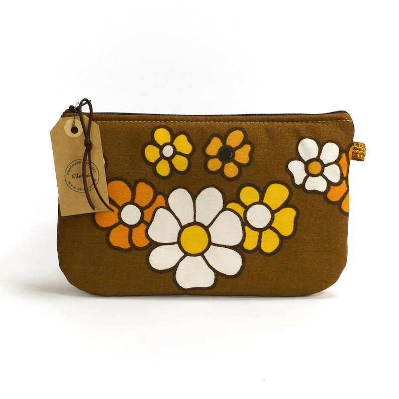 May include: A brown canvas zippered pouch with a floral print featuring yellow, orange, and white daisies. The pouch has a brown leather tag with the text "Ella & Lou" on it.