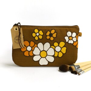 May include: Brown fabric makeup bag with a floral pattern of white, yellow, and orange daisies. The bag has a zipper closure and a brown leather tag with the text "Ella Grace" on it.
