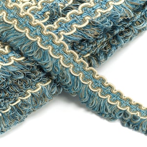 May include: Blue and cream trim with a fringed edge. The trim has a repeating pattern of loops and is woven with a textured yarn.
