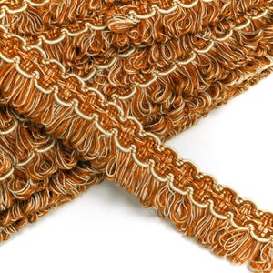 May include: Close-up of a brown and cream braided trim with a fringe. The trim has a woven pattern and is perfect for adding a decorative touch to home decor projects.