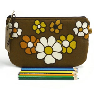 May include: A brown fabric zippered pouch with a floral pattern featuring white, yellow, and orange daisies. The pouch is lying on a white surface with a set of colored pencils in front of it.