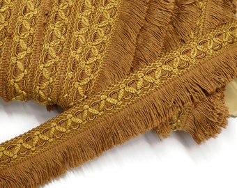 May include: A close-up of brown fringe trim with a gold braided design. The trim is woven with a repeating pattern of loops and leaves.