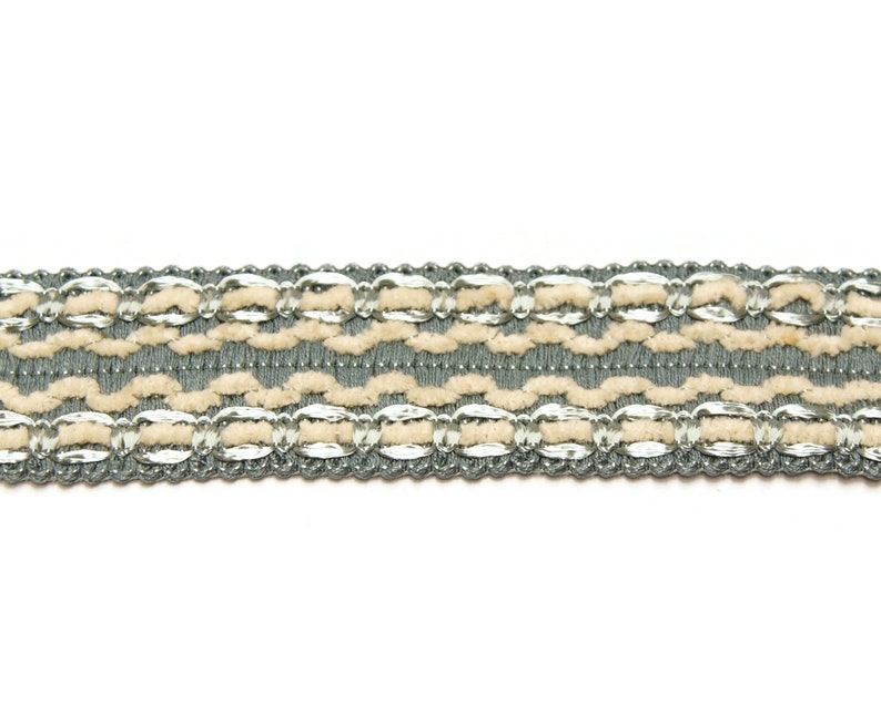 May include: A close-up of a gray and beige trim with a repeating pattern of woven loops and silver accents.