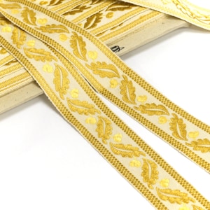 May include: Two rolls of gold and cream coloured ribbon with a leaf pattern. The ribbon is woven with a repeating pattern of leaves and dots.
