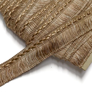 May include: Brown and beige fringe trim with a braided cord detail. The trim is approximately 1 inch wide and has a soft, textured feel.