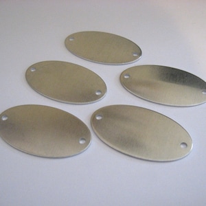 May include: Five silver oval-shaped metal tags with two holes each. The tags are blank and ready for engraving.
