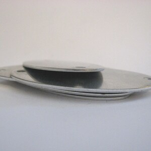 May include: Three silver oval-shaped metal discs stacked on top of each other.