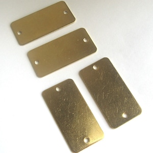 May include: Four rectangular brass tags with holes in the top corners. The tags are blank and have a slightly textured surface.