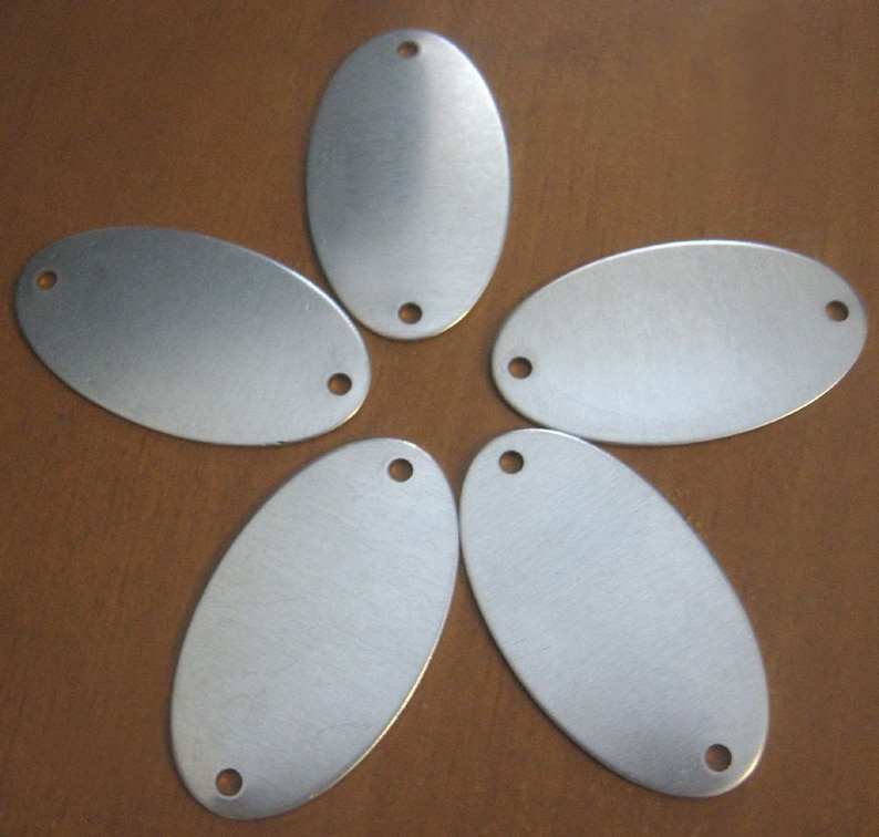 May include: Five silver oval-shaped metal tags with two holes each. The tags are arranged in a star shape on a brown wooden surface.