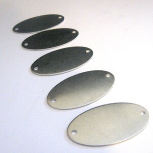 May include: Five silver oval-shaped metal tags with two holes each. The tags are arranged in a row, with the largest tag at the bottom and the smallest tag at the top.