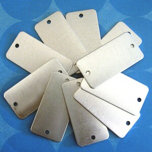 May include: A group of ten silver metal rectangular tags with a hole punched in the top. The tags are arranged in a circle with the holes facing outward.