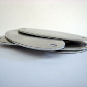 May include: Three silver oval-shaped metal blanks with holes in the center. The blanks are stacked on top of each other.