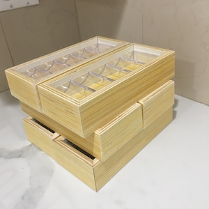 May include: Three stacked wooden boxes with clear plastic inserts and lids. The boxes are made of light-colored wood and have a rectangular shape. The clear lids allow visibility of the contents.