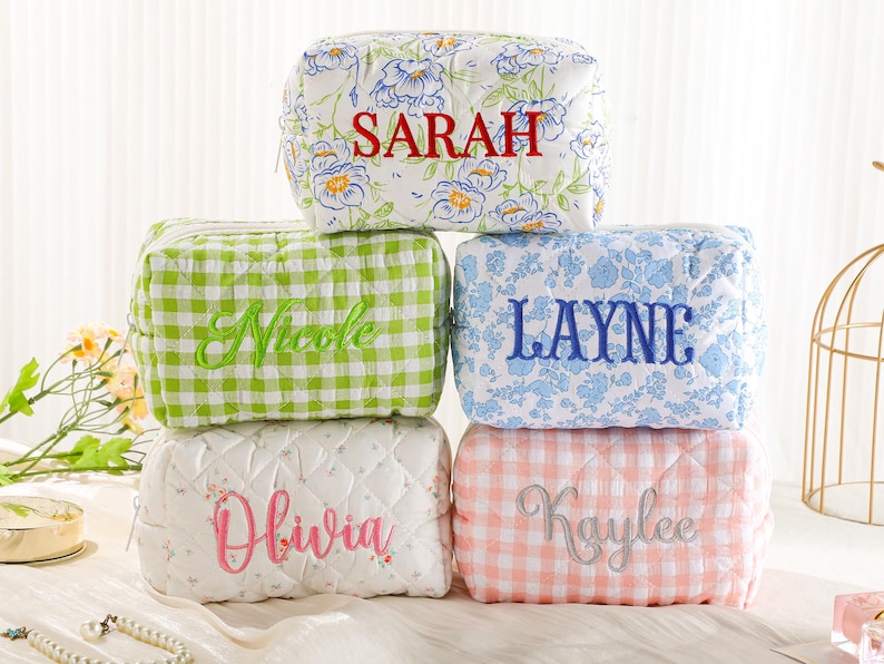 May include: Five quilted cosmetic bags with embroidered names. The bags feature various patterns, including floral, gingham, and a quilted design. The names embroidered on the bags are Sarah, Nicole, Layne, Olivia, and Kaylee.