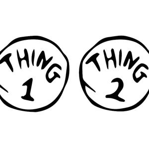 以下が含まれることがあります： 丸い黒と白のサインが2つあり、丸みを帯びたフォントで「THING」と書かれています。1つのサインは「THING 1」、もう1つは「THING 2」と書いてあります。