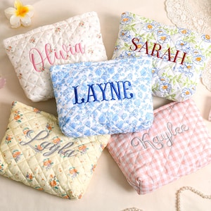 May include: Five quilted cosmetic bags with embroidered names. The bags feature floral and gingham patterns in white, blue, yellow, and pink. Names embroidered include "Olivia", "Sarah", "Layne", "Layla", and "Kaylee".