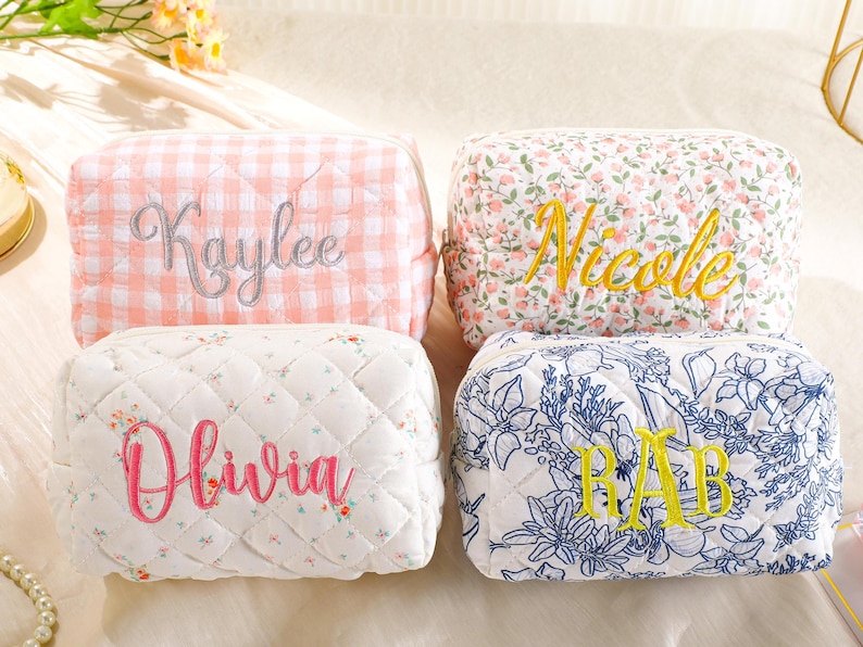 May include: Four quilted cosmetic bags with embroidered names. One is pink gingham with "Kaylee" in silver, another has a floral pattern with "Nicole" in yellow, a third is white with "Olivia" in pink, and the last is blue floral with "RAB" in yellow.