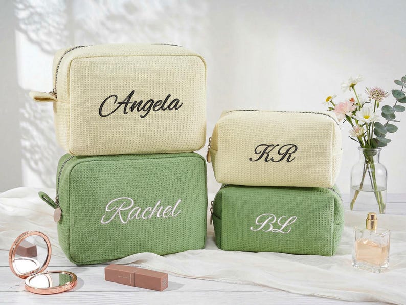 May include: Four rectangular waffle-textured toiletry bags in cream and sage green. The two larger bags feature the names Angela and Rachel embroidered in script, while the two smaller bags feature the initials KR and BL in script.