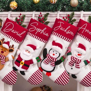 Könnte beinhalten: Vier personalisierte Weihnachtsstrümpfe mit den Namen David, Sophia, Jackson und Amelia. Jeder Strumpf ist weiß mit roten Streifen und einem roten Bund. Festliche Figuren sind Rentier, Weihnachtsmann, Pinguin und Schneemann.