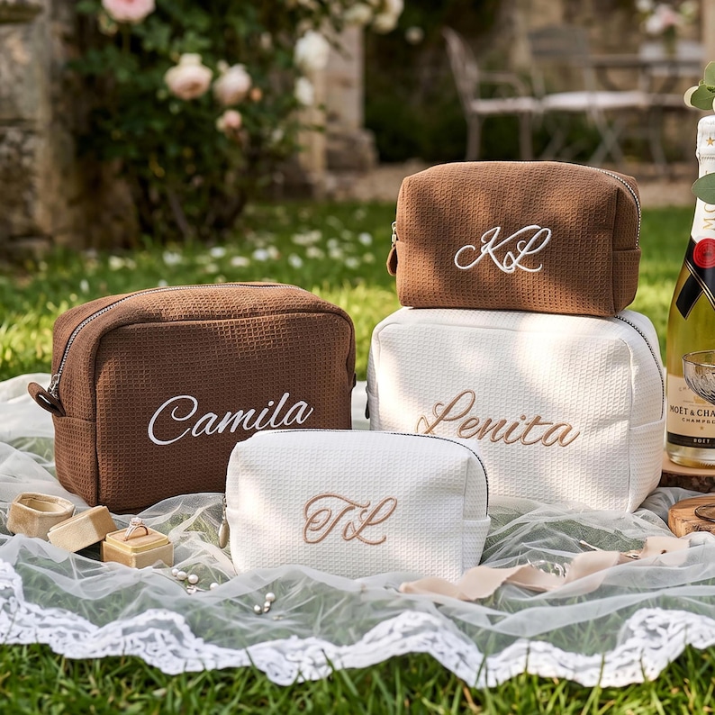 May include: Three rectangular cosmetic bags with a textured waffle-weave fabric. One brown bag features the name Camila in white embroidery. A second brown bag displays the initials KL in white. A white bag features the name Lenita and initials TL.