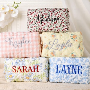 May include: A stack of personalized cosmetic bags in various floral and patterned designs. Each bag is embroidered with a name in a contrasting color. The bags are in shades of red, pink, yellow, and blue, with white floral accents.