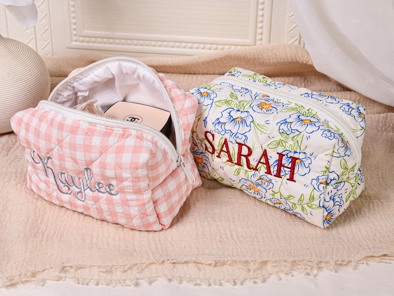May include: Two personalized cosmetic bags. One is pink and white gingham with "Kaylee" embroidered in cursive. The other is white with blue floral print and "SARAH" embroidered in red. Both have zippers.