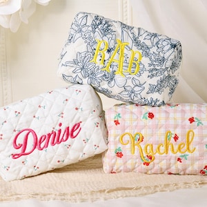 May include: Three quilted cosmetic bags with embroidered names and initials. One bag is white with a cherry pattern and the name "Denise" in pink. Another has a floral pattern with yellow initials. The third is pink with a floral pattern and the name "Rachel" in yellow.