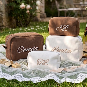 May include: Three rectangular waffle-textured cosmetic bags in brown and white. One brown bag features the white embroidered name Camila. One white bag features the brown embroidered name Lenita. One small white bag features the brown monogram TL.