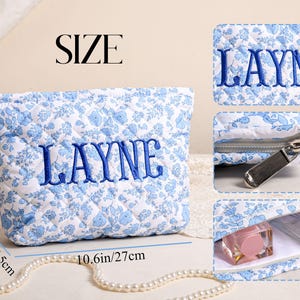 May include: A quilted cosmetic bag with a blue floral pattern and the name "LAYNE" embroidered in blue. The bag is 10.6 inches long, 6.9 inches high, and 2.6 inches wide. It has a zipper closure and is designed to hold makeup and other beauty products.