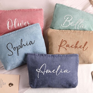 May include: Five corduroy cosmetic bags in various colors: pink, blue, green, tan, and navy. Each bag has a name embroidered on it in a contrasting color: Oliver, Sophia, Bella, Rachel, and Amelia. The bags are rectangular and have a zipper closure.
