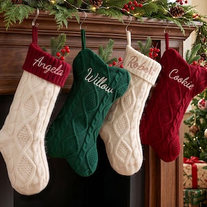 Könnte beinhalten: Vier Weihnachtsstrümpfe aus Zopfstrick, die an Metallhaken hängen. Der erste ist cremefarben mit einem roten Umschlag, bestickt mit "Angela". Der zweite ist dunkelgrün mit "Willow". Der dritte ist cremefarben mit "Robert". Der vierte ist rot mit "Cookie".