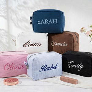 May include: A collection of six rectangular waffle-textured cosmetic bags in blue, white, brown, pink, light blue, and black. Each bag features a personalised name embroidered on the front: Sarah, Lenita, Camila, Olivia, Rachel, and Emily.