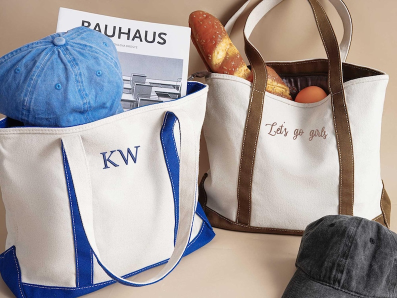 Peut inclure: Deux sacs fourre-tout en toile blanche avec des anses bleues et brunes. Un sac a les initiales "KW" brod&eacute;es sur le devant en fil bleu. L'autre sac a le texte "Let's go girls" brod&eacute; sur le devant en fil brun.