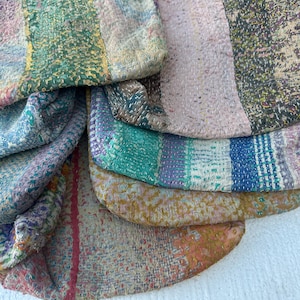Könnte beinhalten: Ein Stapel bunter, handgefertigter Stoffbeutel. Jeder Beutel hat ein einzigartiges Patchwork-Design mit verschiedenen Farben wie Blau, Grün, Rosa und Gelb. Die Beutel scheinen aus recycelten Materialien hergestellt zu sein.