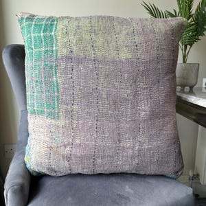 May include: A large, square, patchwork pillow with a green and purple color scheme. The pillow is made of a soft, textured fabric and has a subtle sheen.