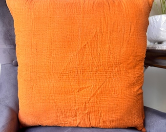 Puede incluir: Un cojín cuadrado naranja con una superficie texturizada. El cojín está colocado sobre una silla tapizada gris. El color del cojín es un naranja vibrante y sólido, y la tela parece tener una textura arrugada. Dimensiones: aproximadamente 40 cm x 40 cm.