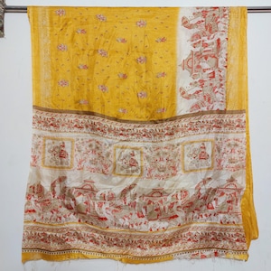 May include: A yellow and white silk sari with a traditional Indian design. The sari has a border with elephants and other animals. The sari is a traditional Indian garment worn by women.