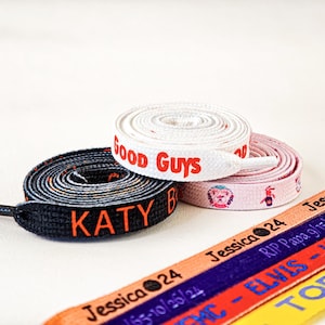 Puede incluir: Cordones de zapatos en varios colores, incluyendo negro, blanco, rosa, naranja, morado y amarillo. Algunos cordones están enrollados, otros rectos. El texto incluye "Good Guys", "KATY" y nombres con fechas.