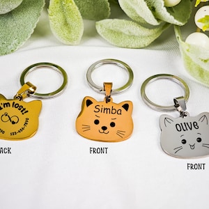 May include: Three cat-shaped pet ID tags with key rings. One is gold with the text "I'm lost!" and a phone number. Another is orange with the name "Simba". The third is silver with the name "Olive".