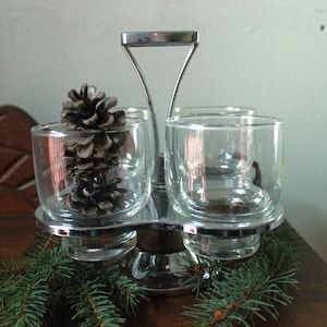 Könnte beinhalten: Ein klarer Glas- und Chrom-Gewürzhalter mit drei Fächern. Ein Fach enthält einen Tannenzapfen. Der Halter hat einen Griff und steht auf einer Holzoberfläche mit Tannenzweigen.