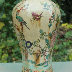 May include: A decorative ceramic vase with a cream-colored background and detailed illustrations of birds, butterflies, and floral elements. The vase features a crackle glaze and a colorful design, with a blue and green base.
