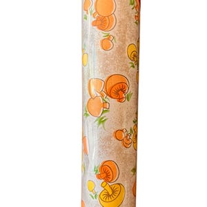May include: A roll of wallpaper featuring a repeating pattern of orange and yellow mushrooms on a light beige background. The mushrooms have detailed caps and stems, with green accents. The roll is wrapped in clear plastic.