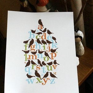 May include: A white card with a brown, blue, and orange alphabet design. Each letter is formed by a silhouette of a bird. The letters are arranged in a tree-like shape.