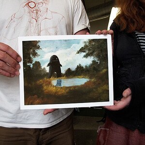 May include: A framed painting of a dark, shadowy figure standing in a forest clearing. The figure has a large, round head and a wide, toothy grin. The painting is set against a backdrop of lush green trees and a small, still pond.