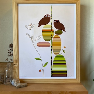 May include: Framed print of a minimalist illustration featuring two brown owls perched on a stack of colorful striped rocks. The background is white with a green plant on the left side of the image.