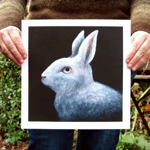 May include: A white rabbit with a black background. The rabbit has a fluffy white coat and a long, pointed nose. The rabbit's eyes are black and its ears are long and floppy.