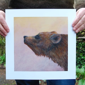 May include: A close-up of a brown bear's head, painted in a realistic style. The bear's head is turned to the side, and its eyes are closed. The background is a soft, pastel pink.