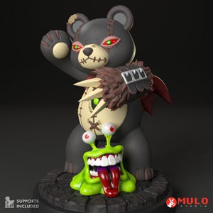 Op de afbeelding: Een zwart-groene teddybeer met gestikte naden en gloeiende rode ogen staat boven een groen, tandenmonster met een lange rode tong. De beer heeft een geklauwde hand met een leren band en metalen gespen. Het monster staat op een ronde basis met een steenachtige textuur.