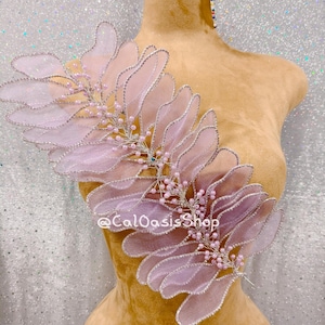 May include: A light pink, decorative floral applique with silver trim and small pink beads. The applique is displayed on a mannequin and features the text "@CalOasisShop".